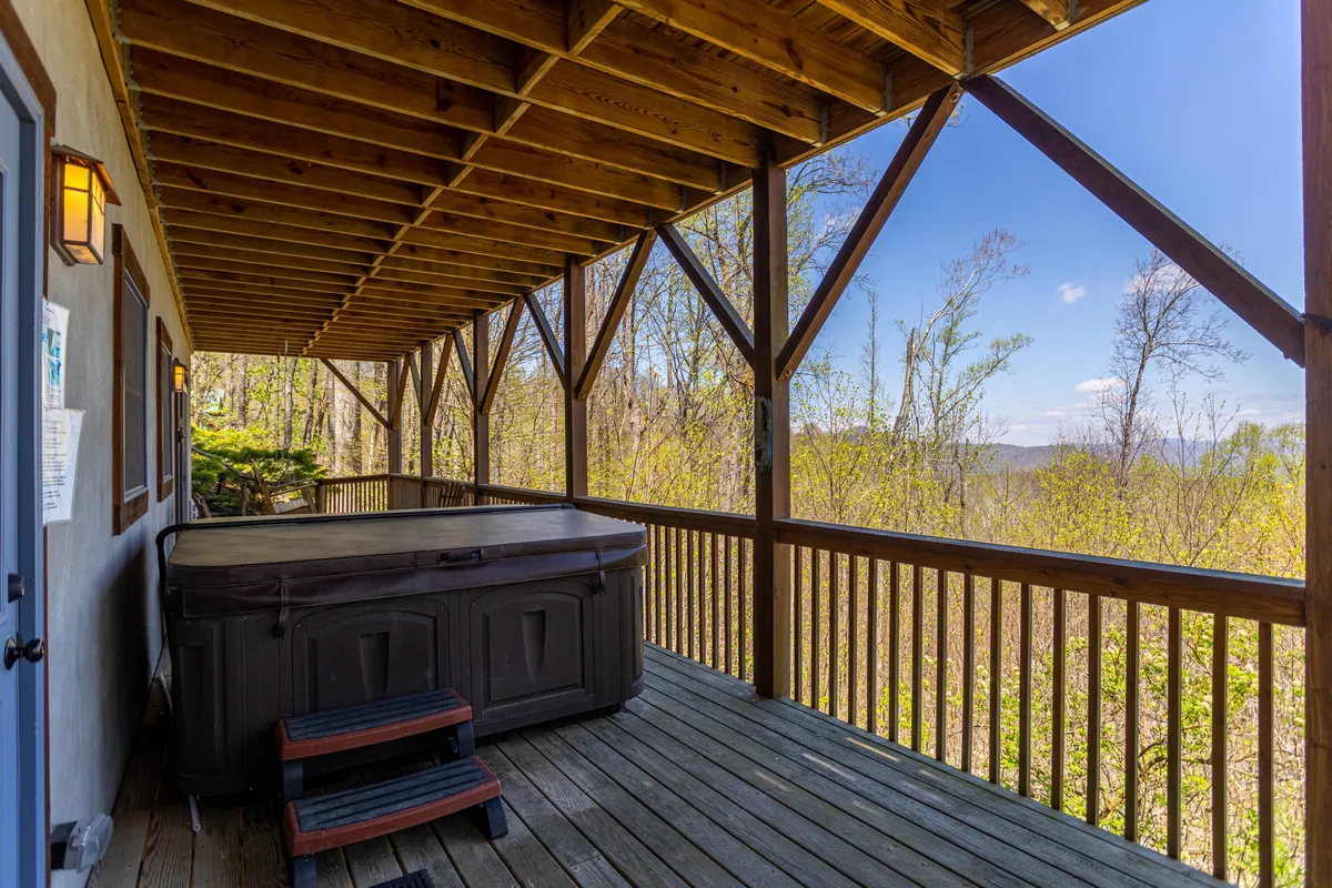An exterior shot featuring a hot tub on a wooden deck surrounded by serene nature. The inviting waters of the tub, coupled with the quiet of the setting, evoke relaxation after a day of adventure. This is an ideal spot for unwinding, stargazing, or sharing stories as a family group.