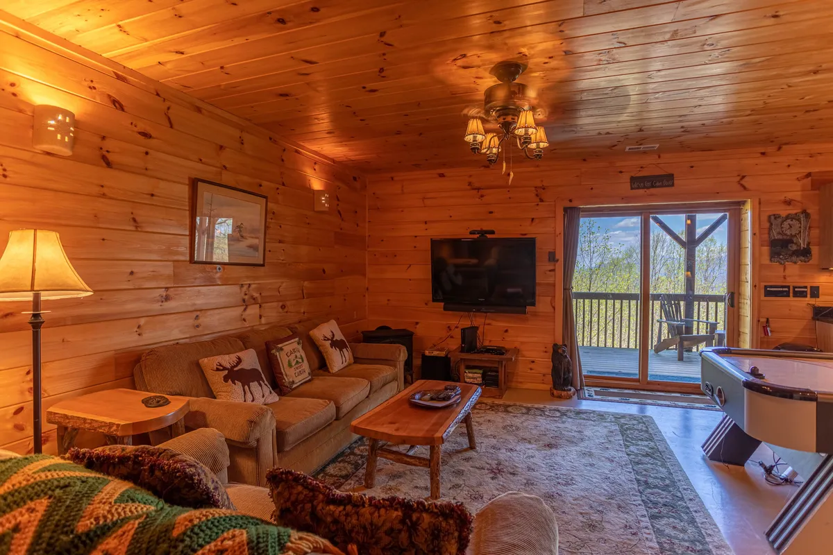 This image shows a cozy living area with a sofa and coffee table oriented toward a television. Most notably, a large sliding door leads directly to a deck, offering a seamless transition between indoor comfort and outdoor adventure. Through the glass, the inviting deck and wooded backdrop are visible, hinting at the natural surroundings just outside.