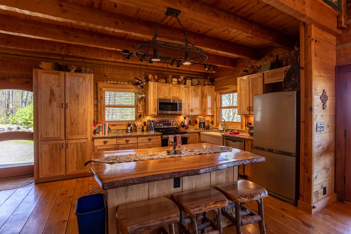 A modern kitchen with a central island, wooden cabinetry, gleaming appliances, and large windows offering glimpses of the outdoors. The setting is bright and welcoming, suggesting a perfect spot for cooking and gathering.