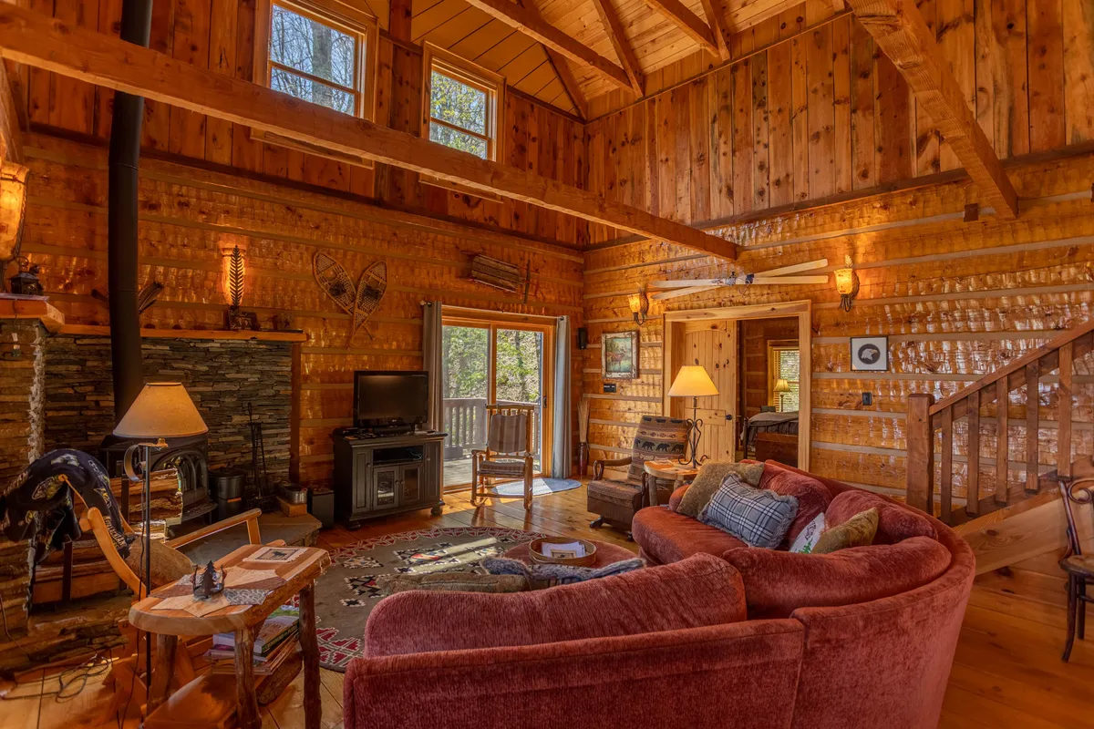 This image features a large, inviting sectional sofa facing a substantial stone fireplace, accented by wooden beams and large windows. The windows allow natural light to flood the space and offer glimpses of the outside winter landscape. The arrangement suggests a welcoming spot for gathering after a day in the snow, with the fireplace promising warmth and coziness.