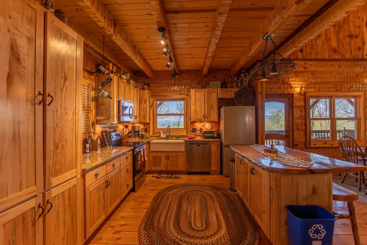 A warmly-lit kitchen with custom wooden cabinetry and granite countertops, centered around a spacious island. Windows provide glimpses of the surrounding landscape, while the layout invites communal cooking and entertaining. The kitchen is well-equipped and designed for gatherings, reflecting both functionality and aesthetic appeal.