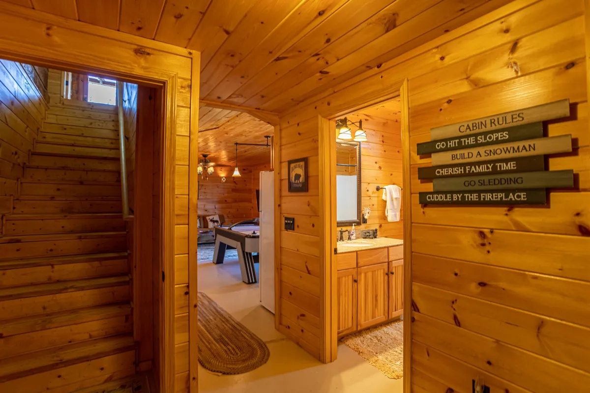This image highlights a wooden staircase and a rug, with a visible sign of cabin rules—a nod to the authentic mountain experience. The cozy, communal space suggests preparations for winter activities and evenings spent together.