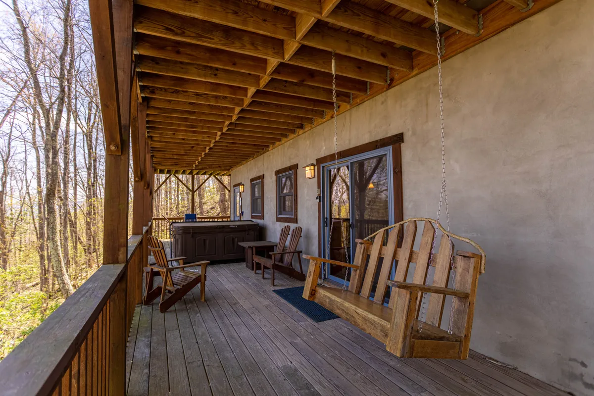 A spacious wooden deck featuring a swinging chair and a bubbling hot tub, both surrounded by wooded scenery. The inviting hot tub overlooks nature, and the deck’s sturdy railings and seating create a tranquil, sheltered spot for relaxation and stargazing.