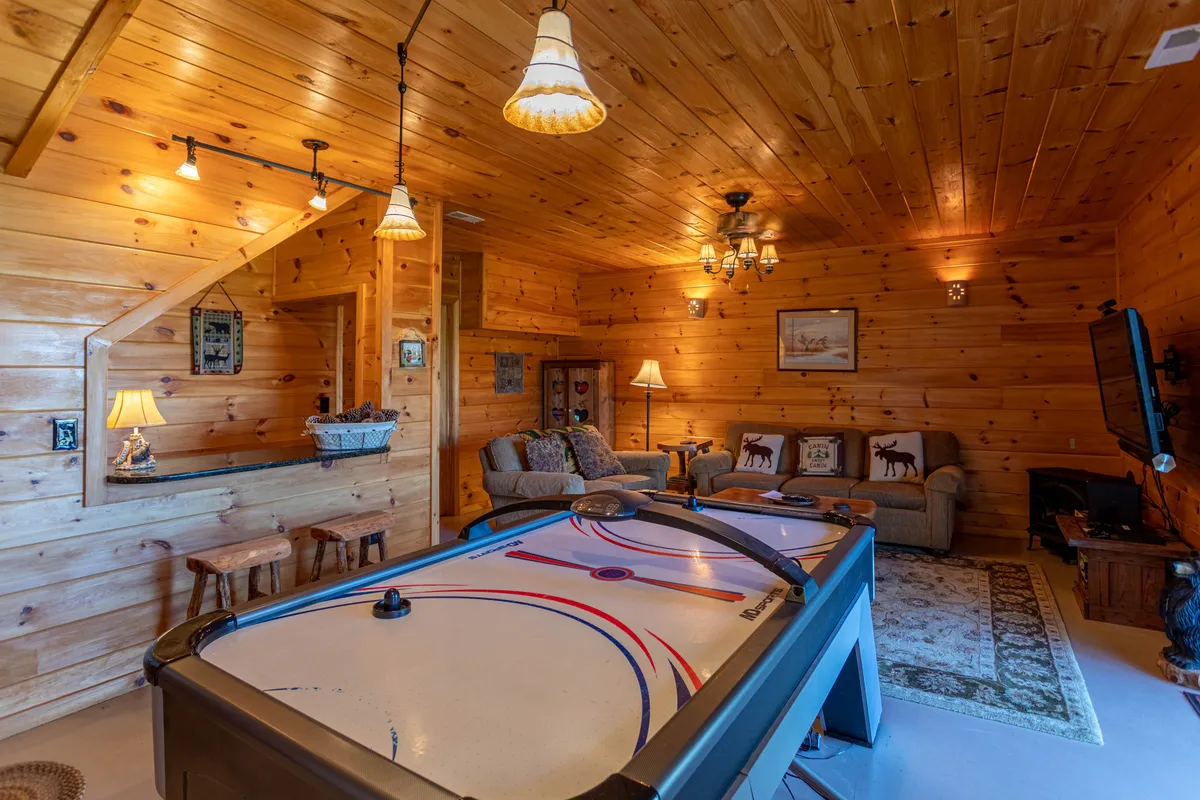 A playful family room highlighted by an air hockey table, comfortable sofa seating, warm wooden walls, and relaxed lighting. The layout encourages family interaction, games, and cozy relaxation after a day of adventure.