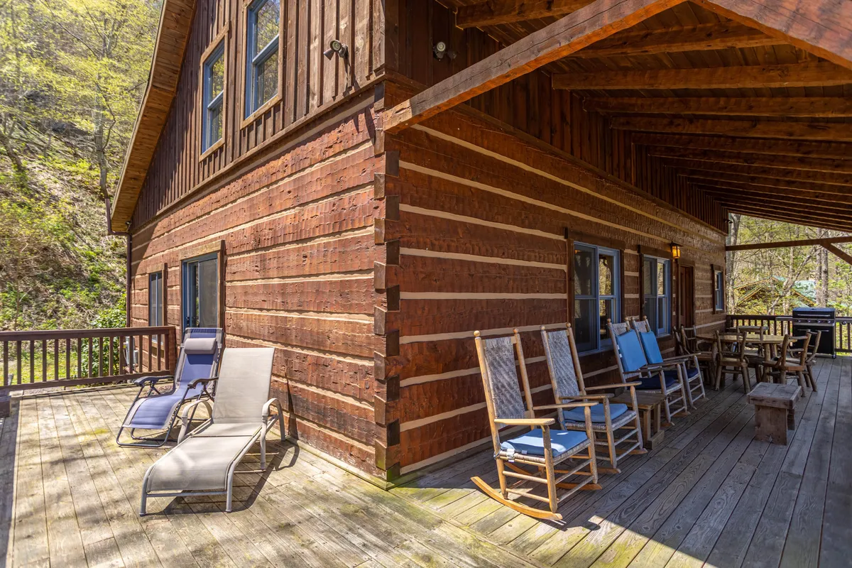 This image shows a welcoming wooden deck outfitted with classic rocking chairs overlooking lush trees and the log cabin structure. The scene captures the essence of relaxing outdoors while enjoying the mountain air, with plenty of space for families to gather and take in the views.