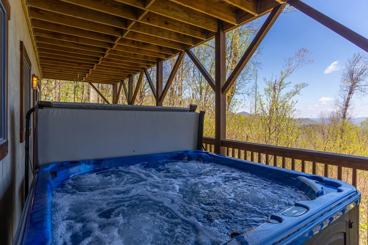 An exterior view of the wooden deck, featuring a bubbling hot tub surrounded by natural beauty. The scene conveys relaxation, with the hot tub perfectly positioned for stargazing or unwinding after a day of games and activities.